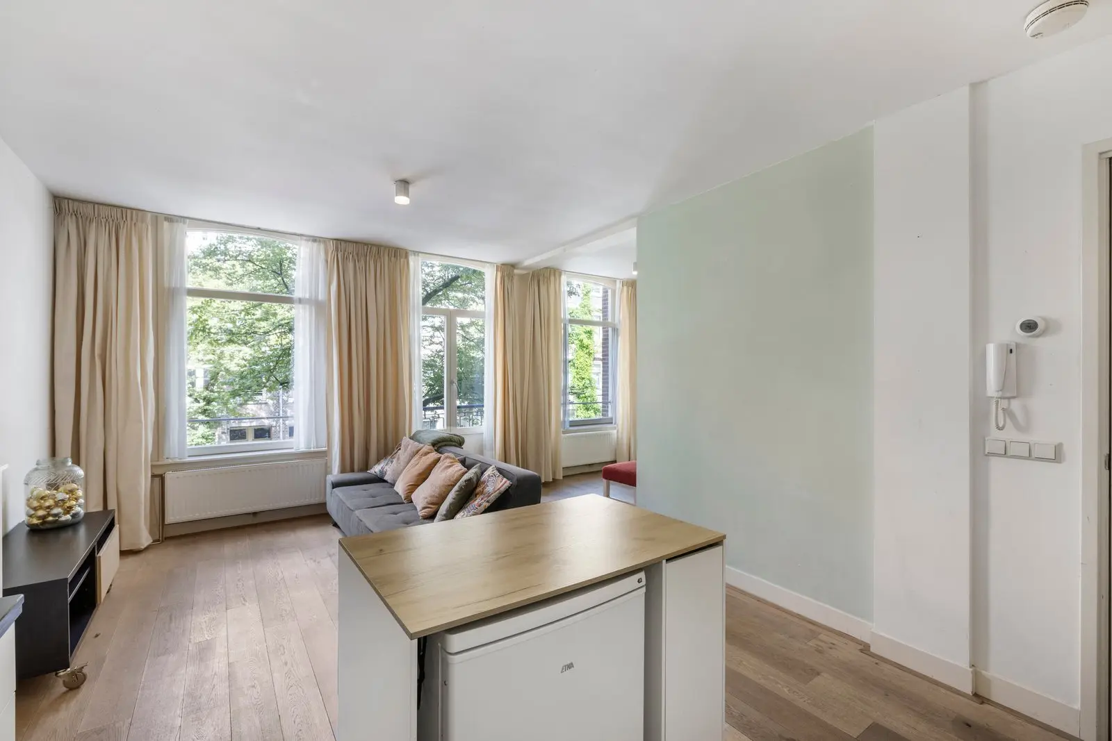 Woonkamer met bank en tafel bij de hoge ramen