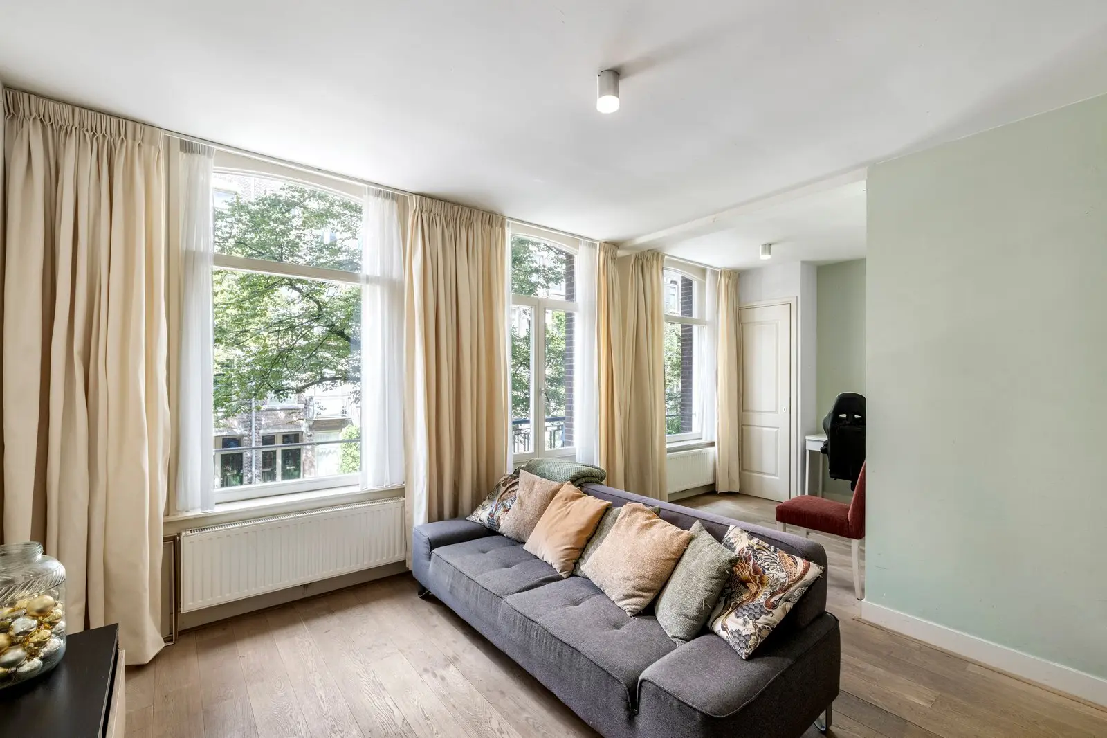 Woonkamer met grijze bank onder de hoge ramen