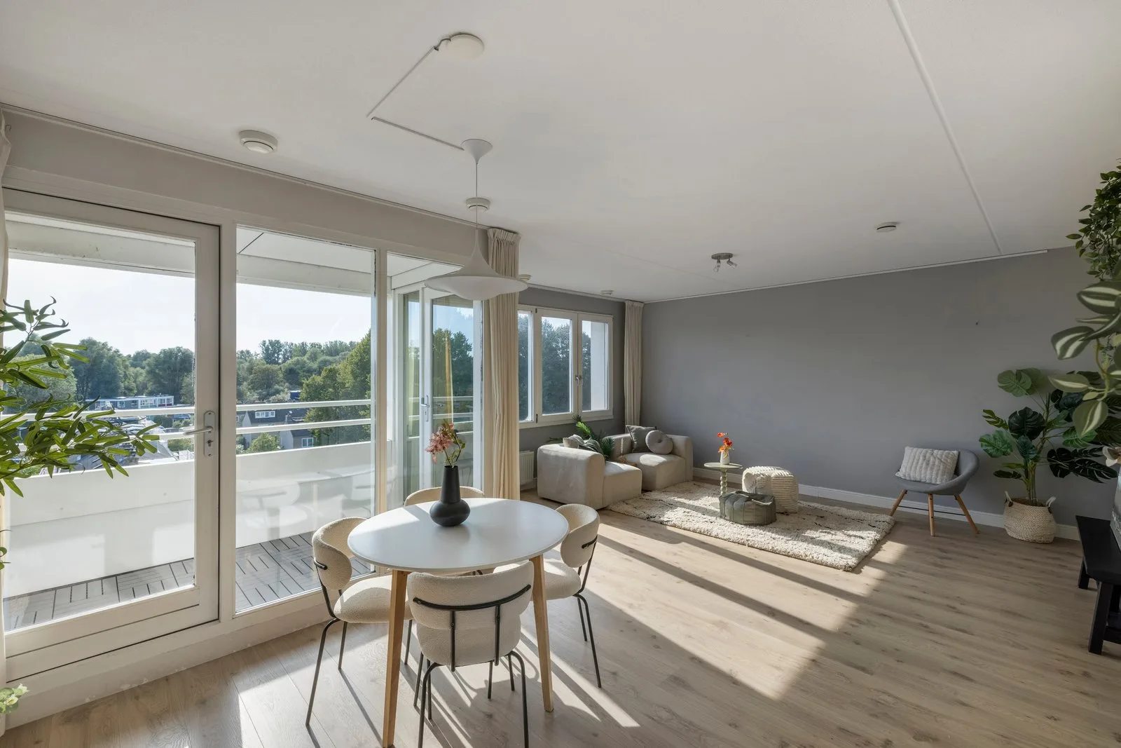 Woon-eetkamer met grote raampartijen en balkondeuren, met de eettafel en de zithoek in het licht