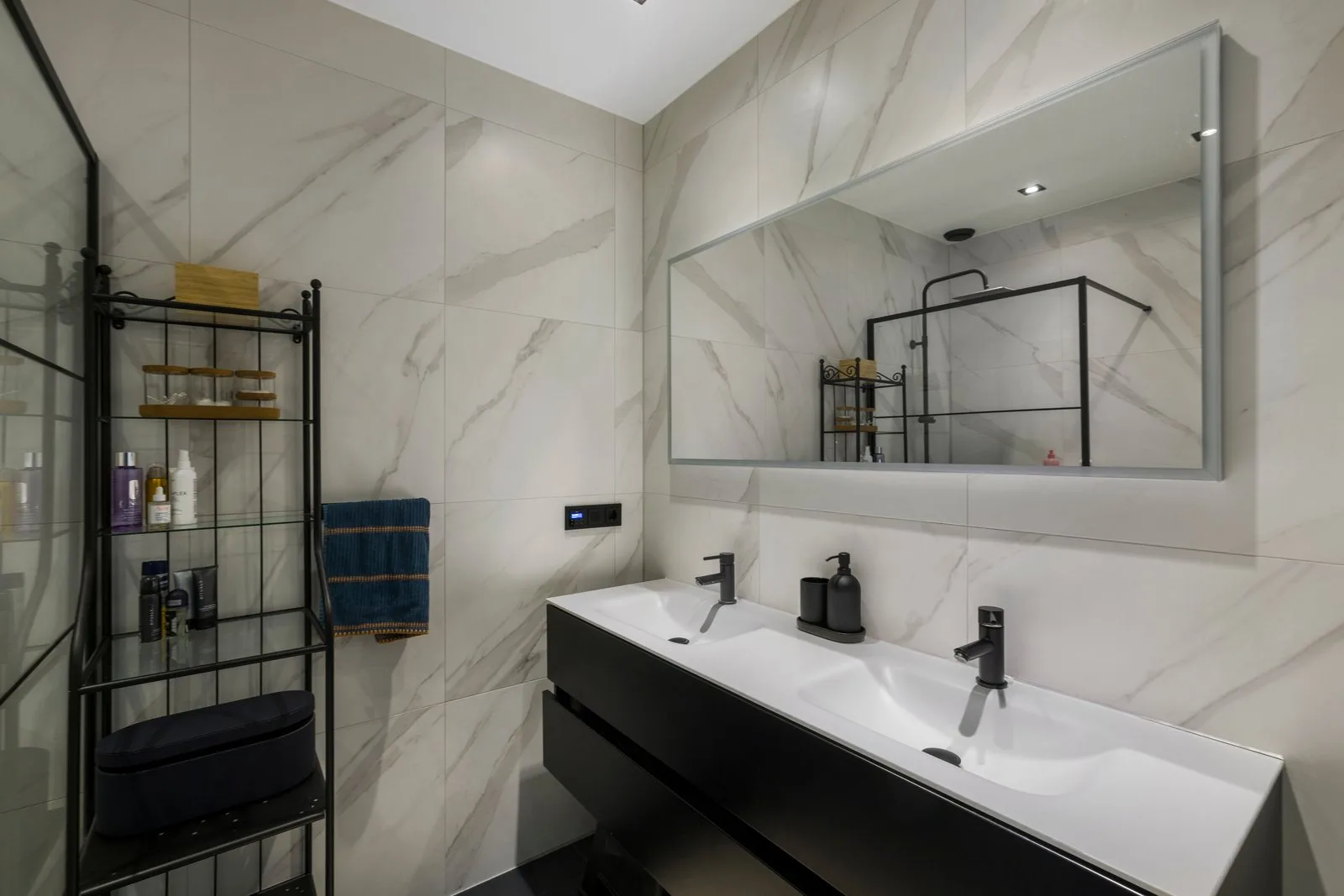 Badkamer met marmerlook tegels, een zwart dubbel wastafelmeubel en de douche in de spiegel