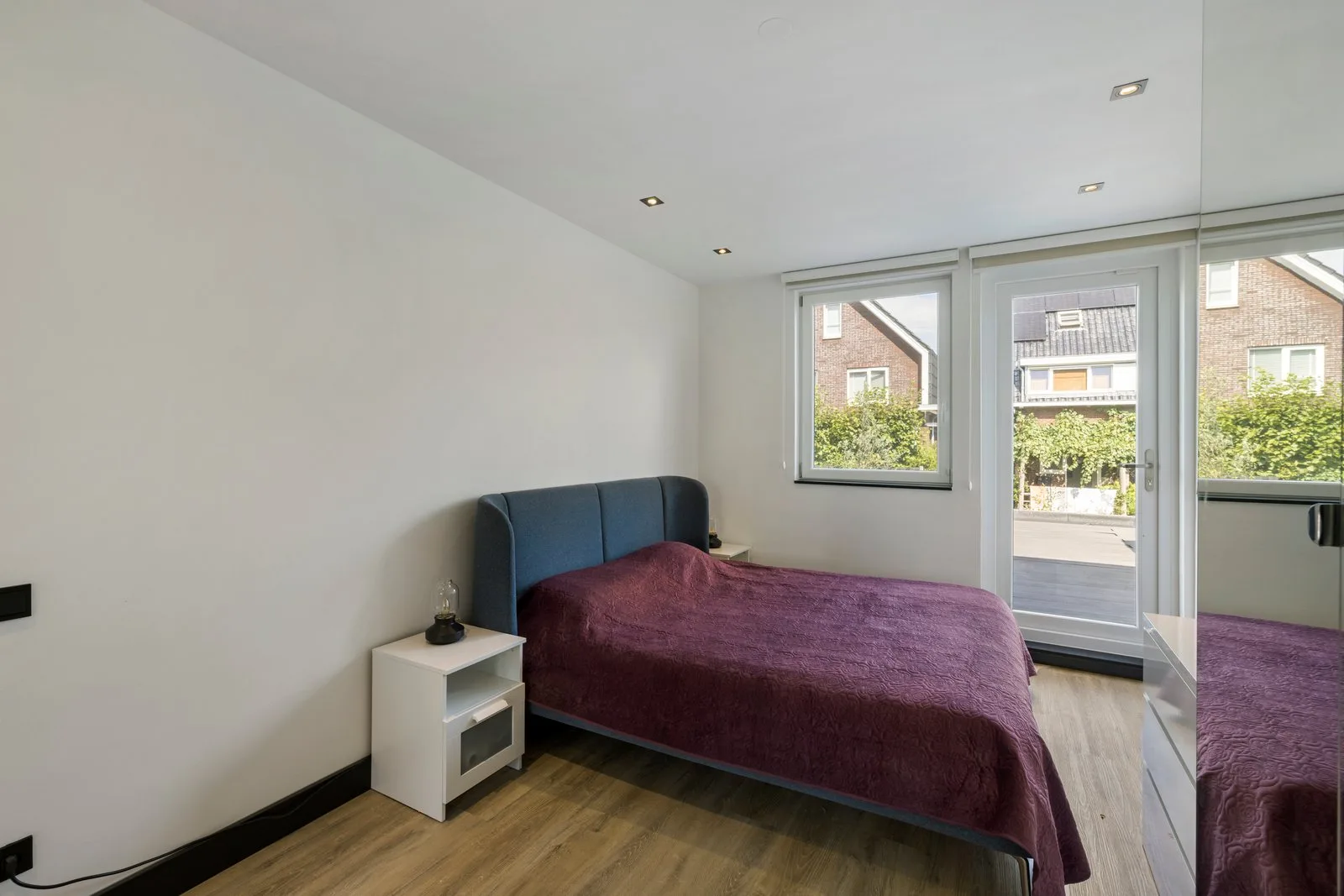Tweepersoonsbed met blauw hoofdbord in de slaapkamer en een glazen deur naar het dakterras