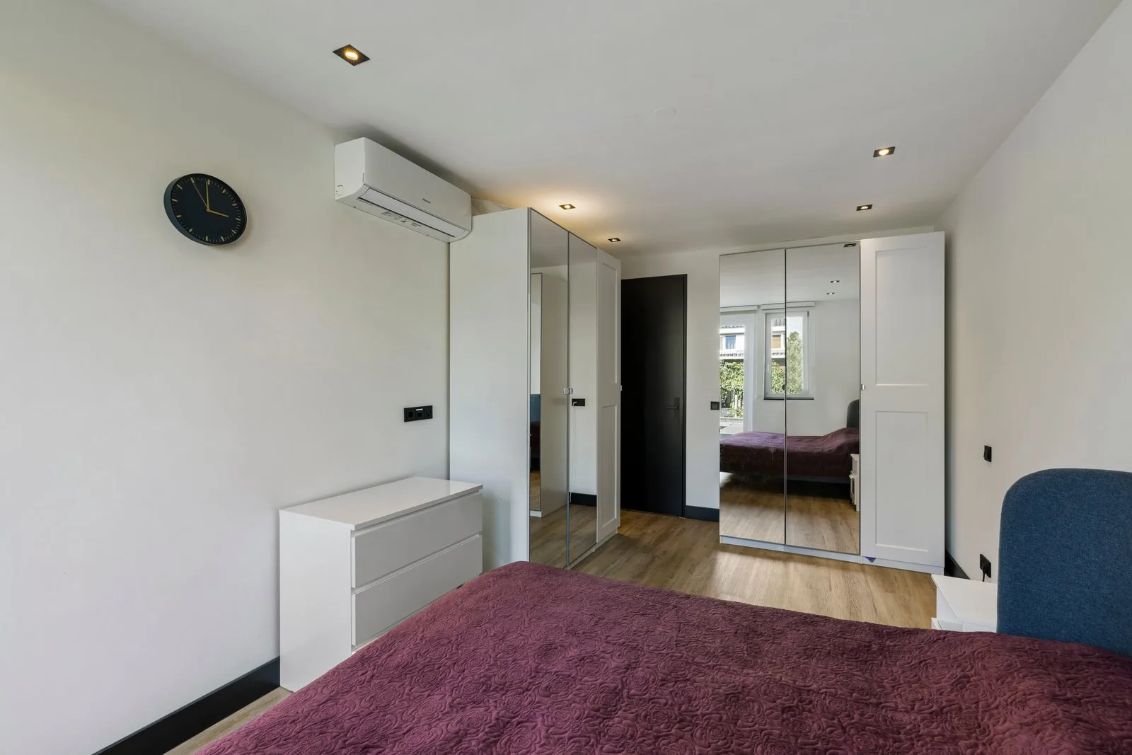 Slaapkamer met spiegeldeuren op de kasten, een witte ladekast en airconditioning aan de wand