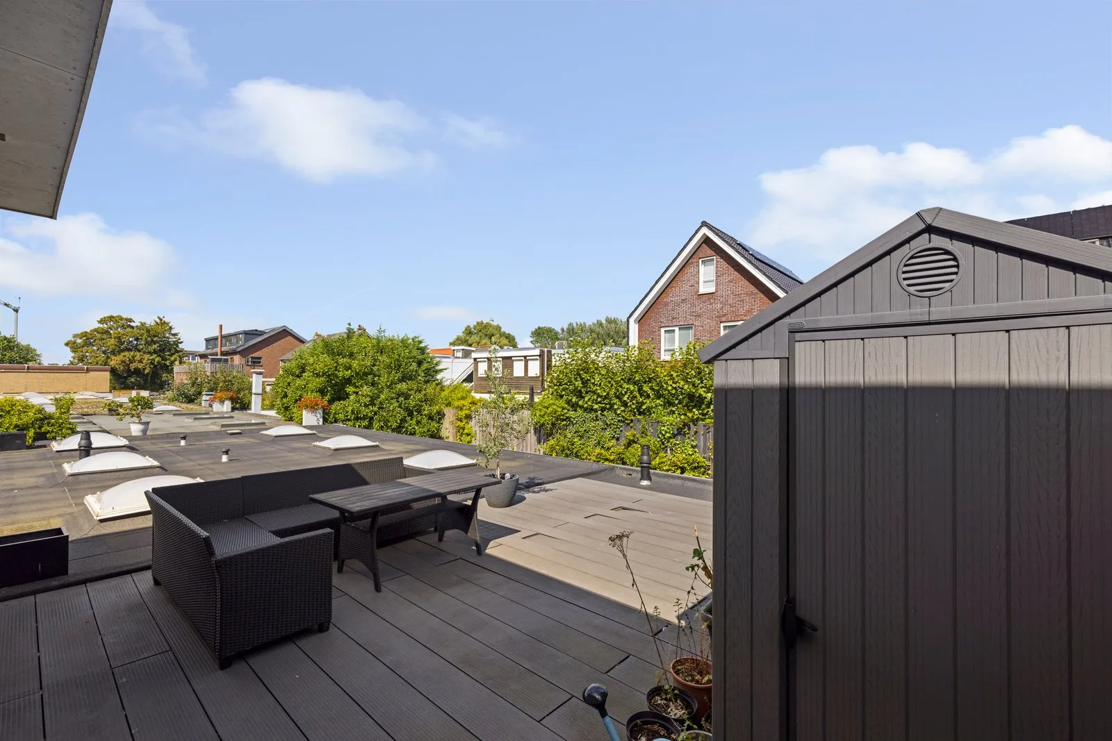 Zwarte loungeset en een kunststof berging op het dakterras, naast een plat dak met lichtkoepels