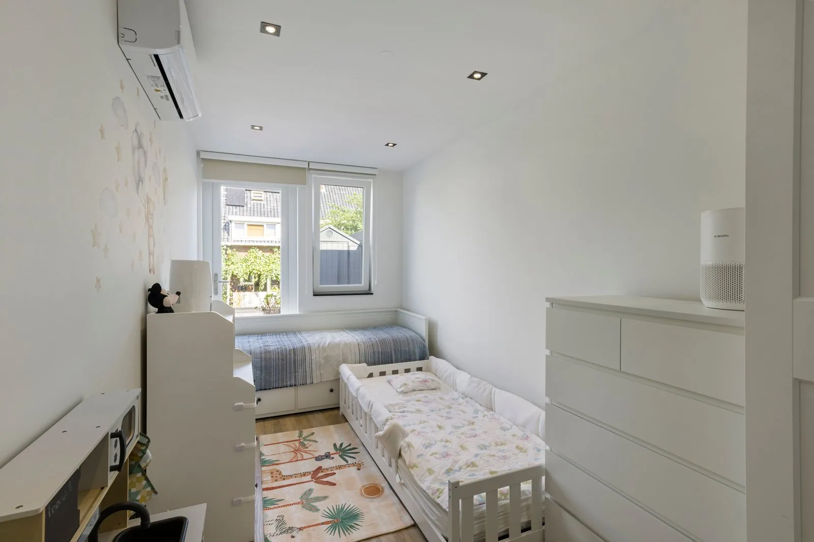 Twee bedden in de kinderkamer, met een speelkleed met dieren en een witte ladekast