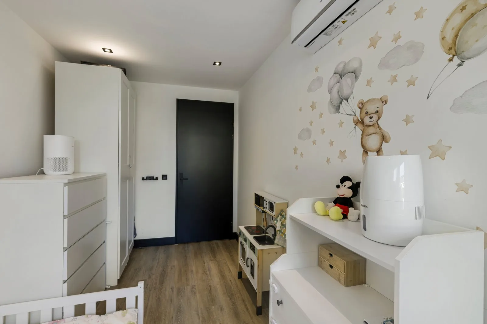 Kinderkamer met muurstickers van een beer met ballonnen, een houten speelkeuken en een zwarte deur