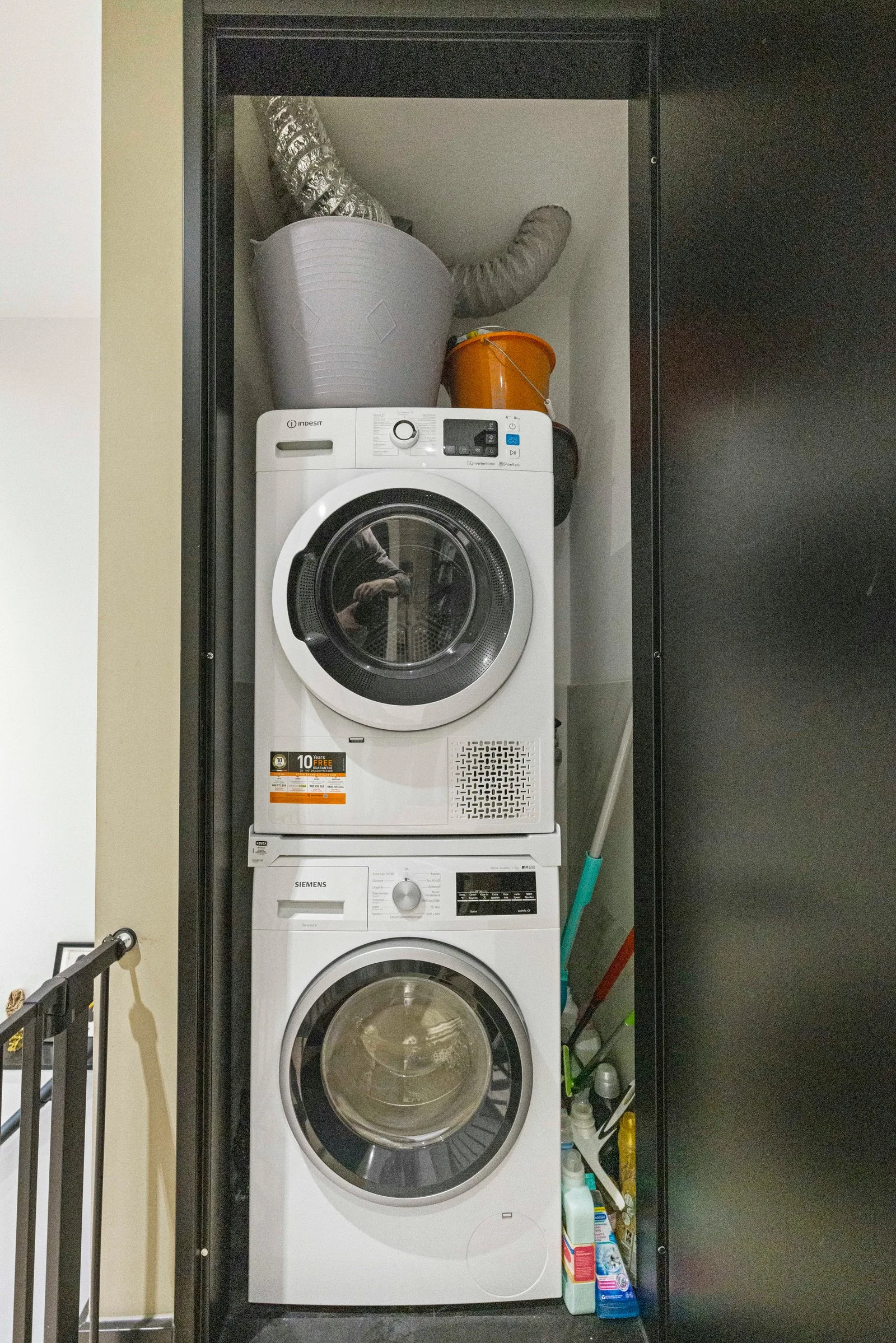 Wasmachine en droger boven elkaar in een kast achter een zwarte deur