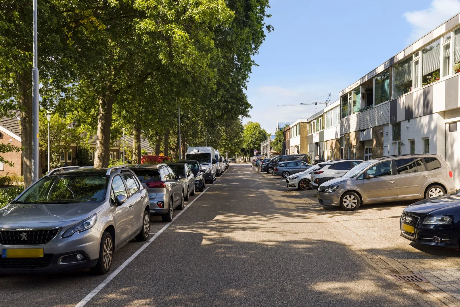 Rij panden met twee bouwlagen aan de straat, met geparkeerde auto's en bomen aan de overkant