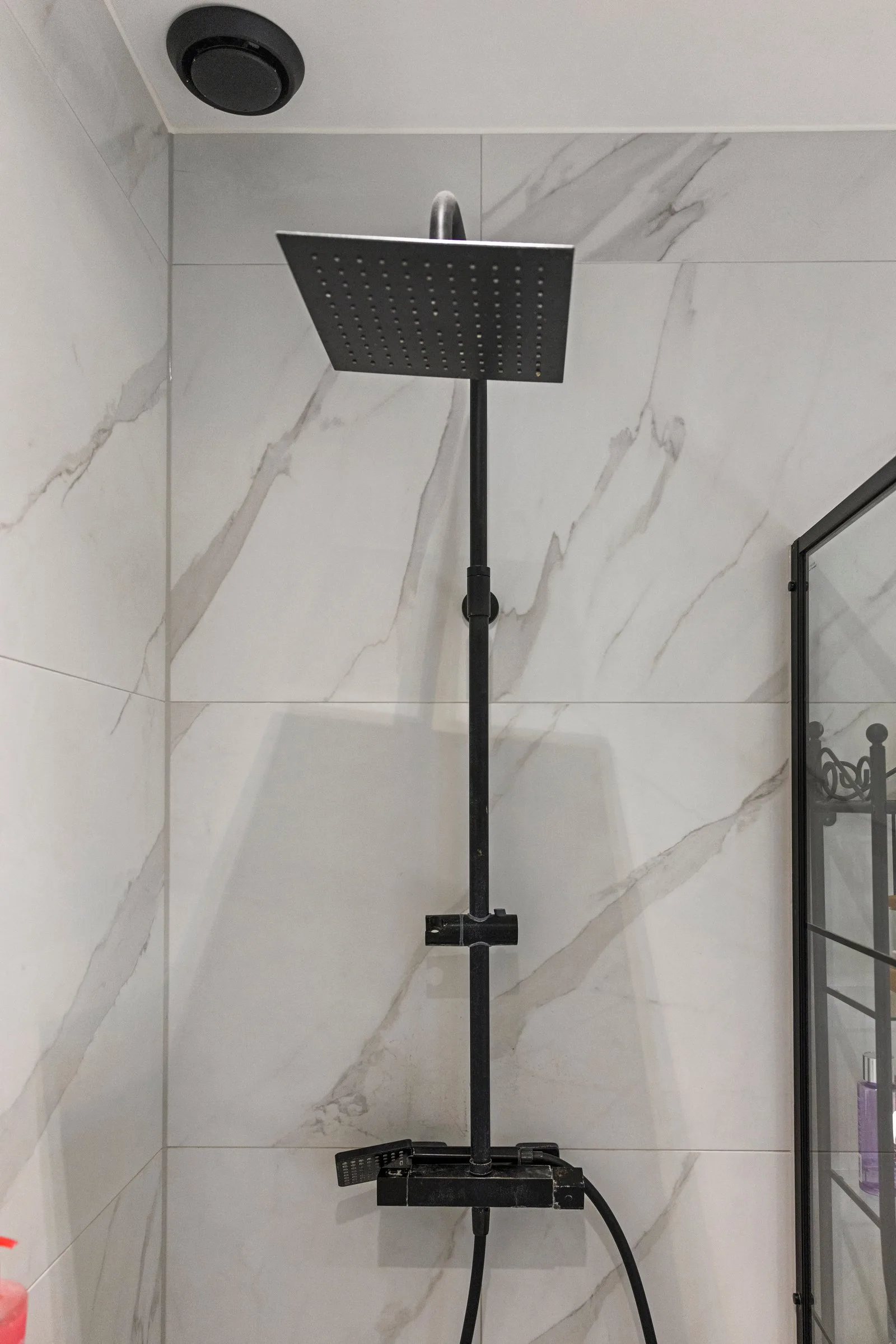 Douchehoek met vierkante zwarte regendouche en handdouche tegen marmerlook tegels, rechts het glazen scherm