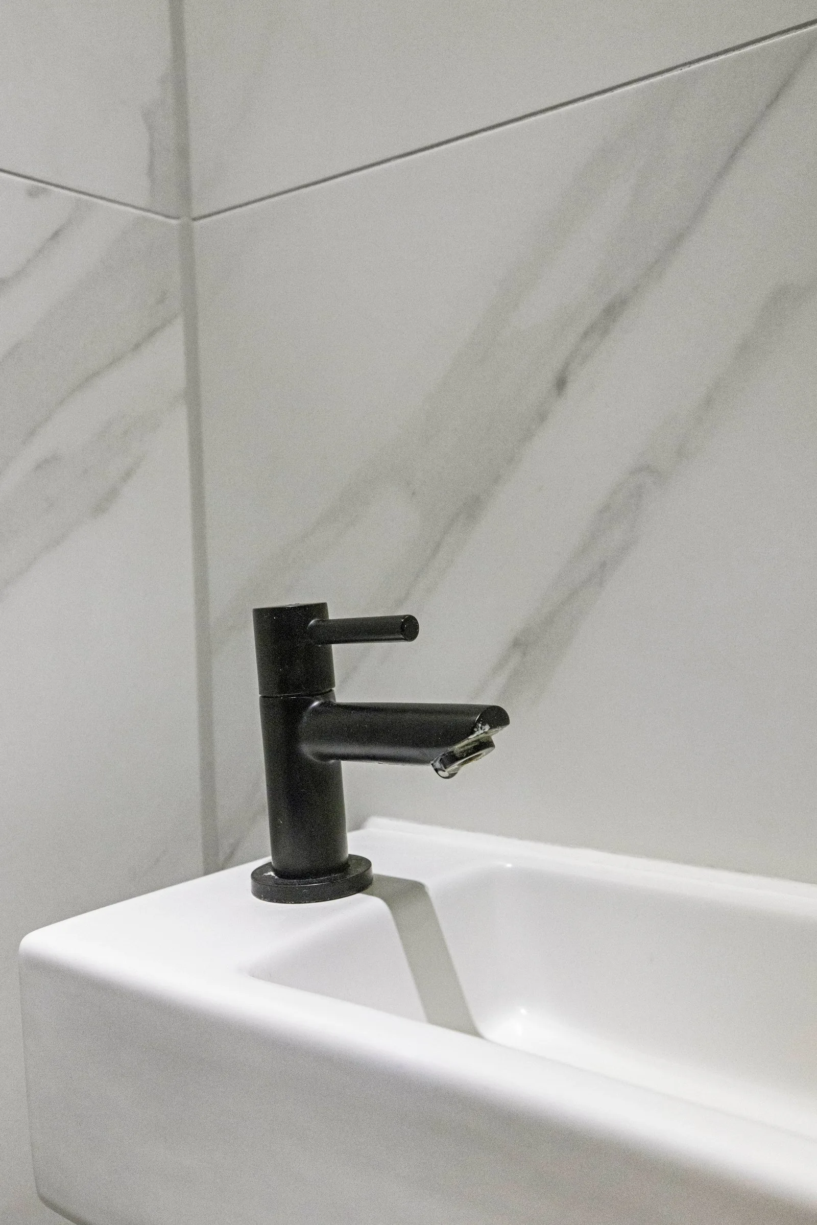 Toilet met rechthoekig fonteintje en zwarte kraan tegen wandtegels met marmerlook
