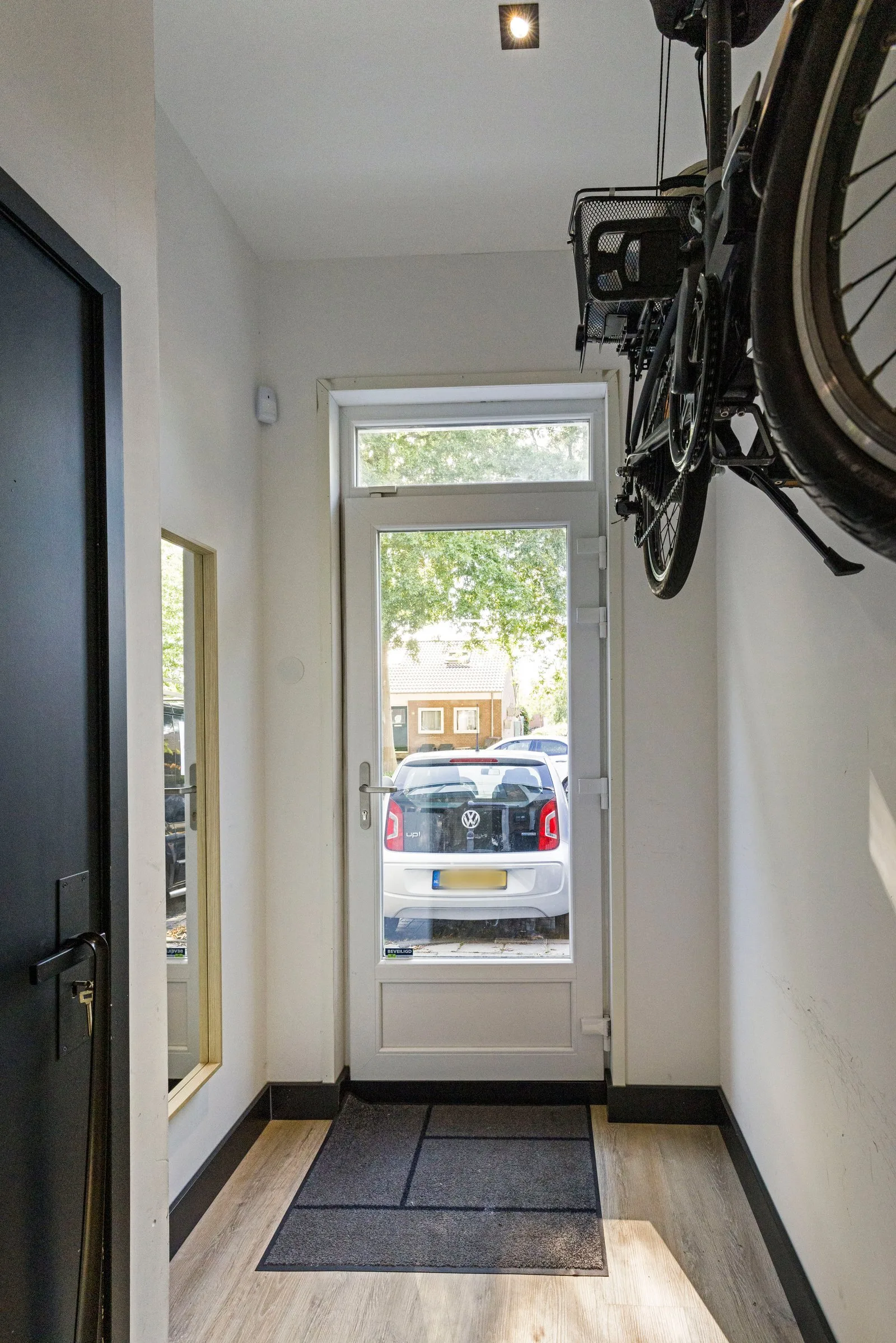 Entree met glazen voordeur en bovenlicht, zicht op de straat en een fiets aan de wand