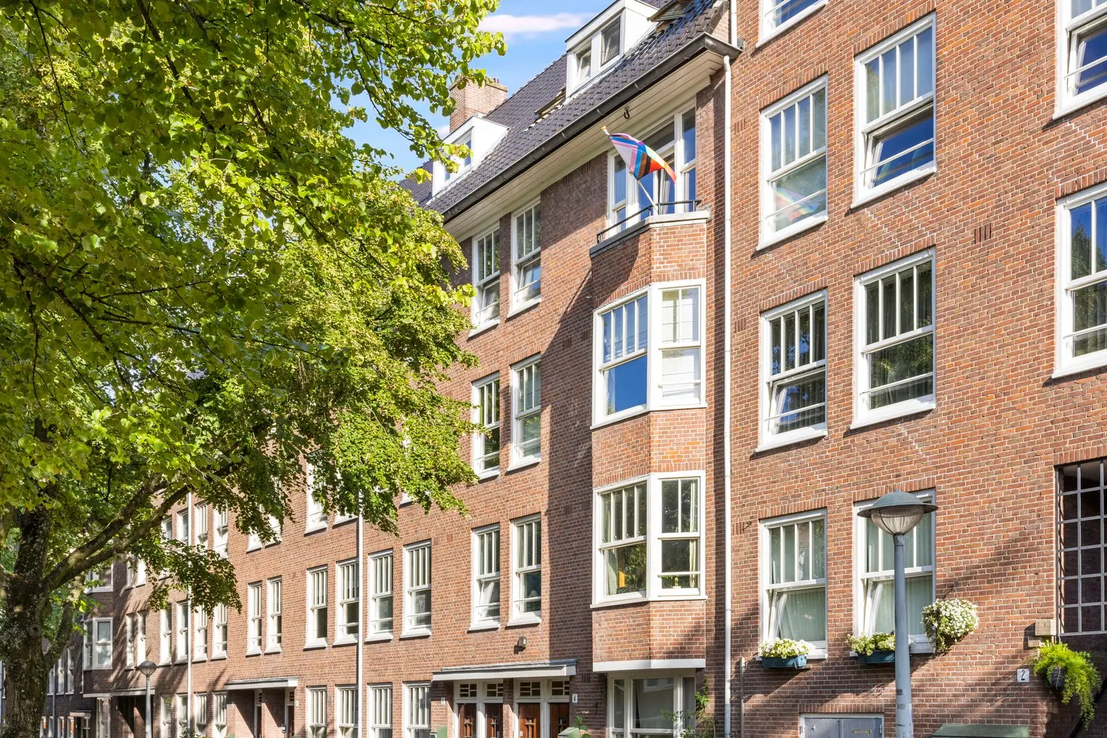 Bakstenen gevel in Amsterdamse Schoolstijl, met een boom voor het pand