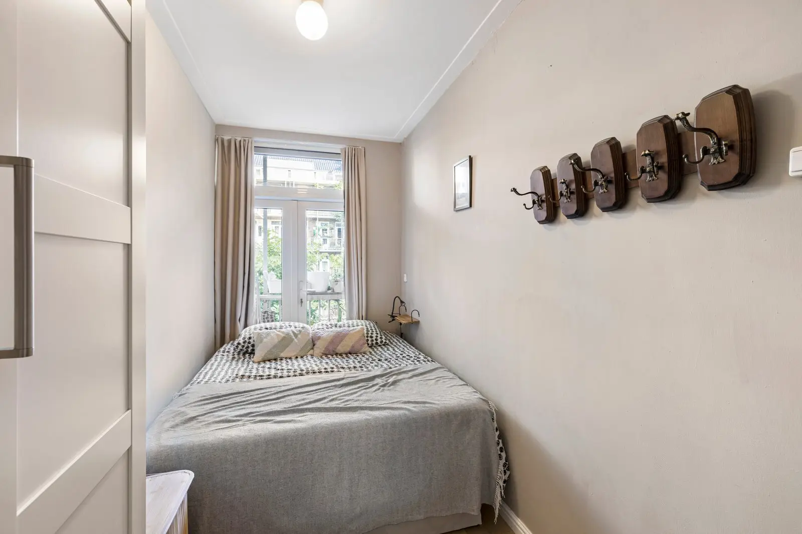 Slaapkamer met bed en een rij houten kapstokhaken