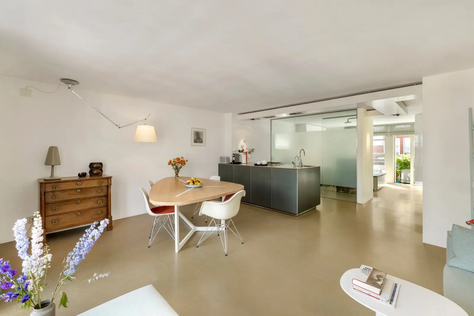 Woonkamer met eettafel, kuipstoelen en een houten ladekast, met het kookeiland op de achtergrond