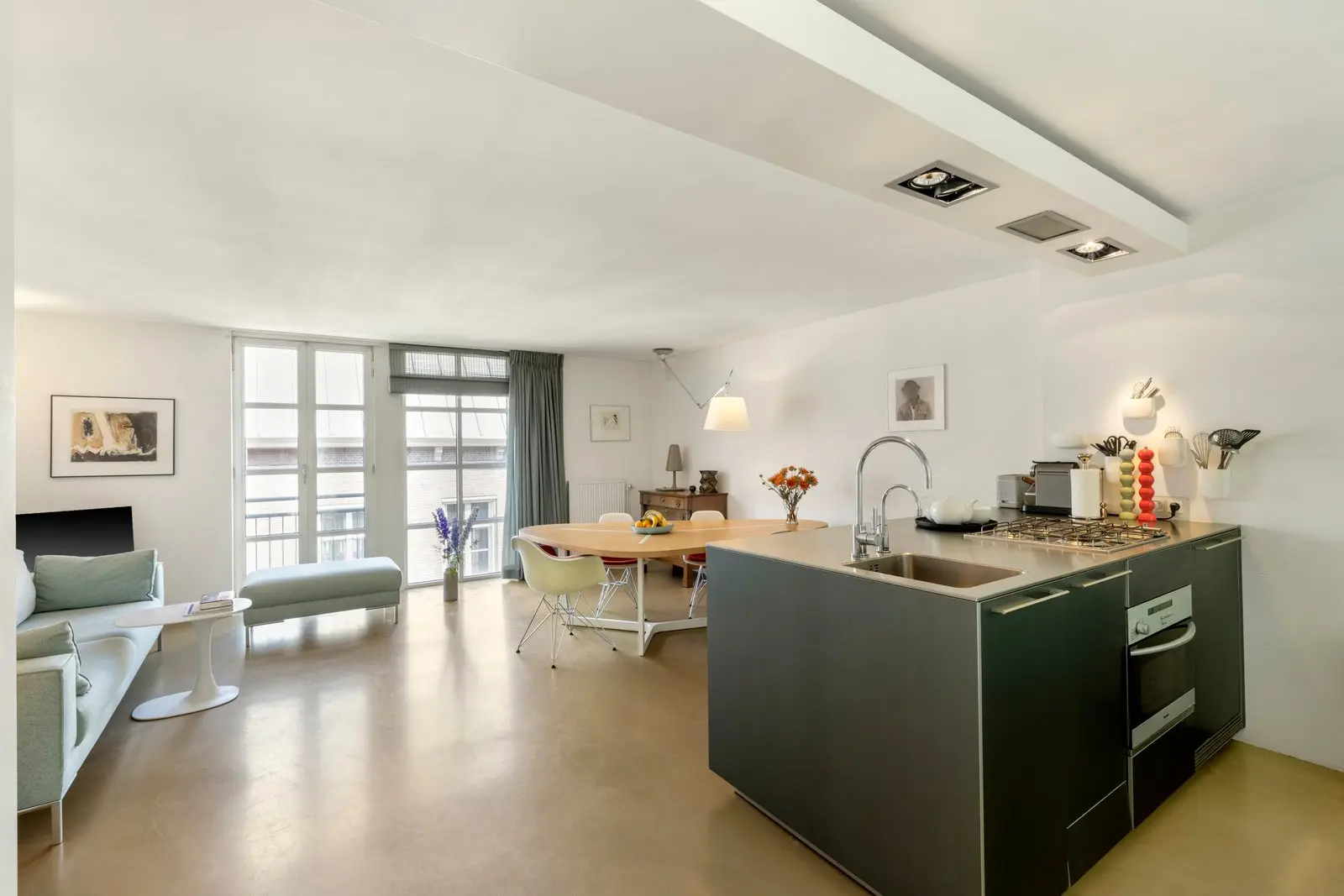 Open keuken met kookeiland en zicht op de eettafel, de bank en de hoge ramen