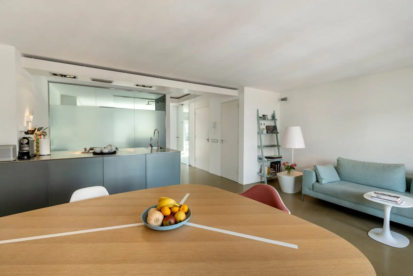 Houten eettafel met fruitschaal, links het kookeiland en rechts de bank met een staande lamp