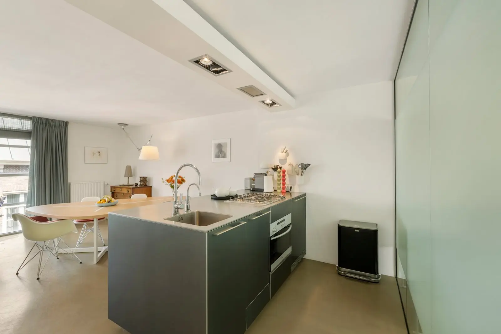 Ingebouwde oven en spoelbak in het kookeiland, met rechts een matglazen wand en de eettafel achterin