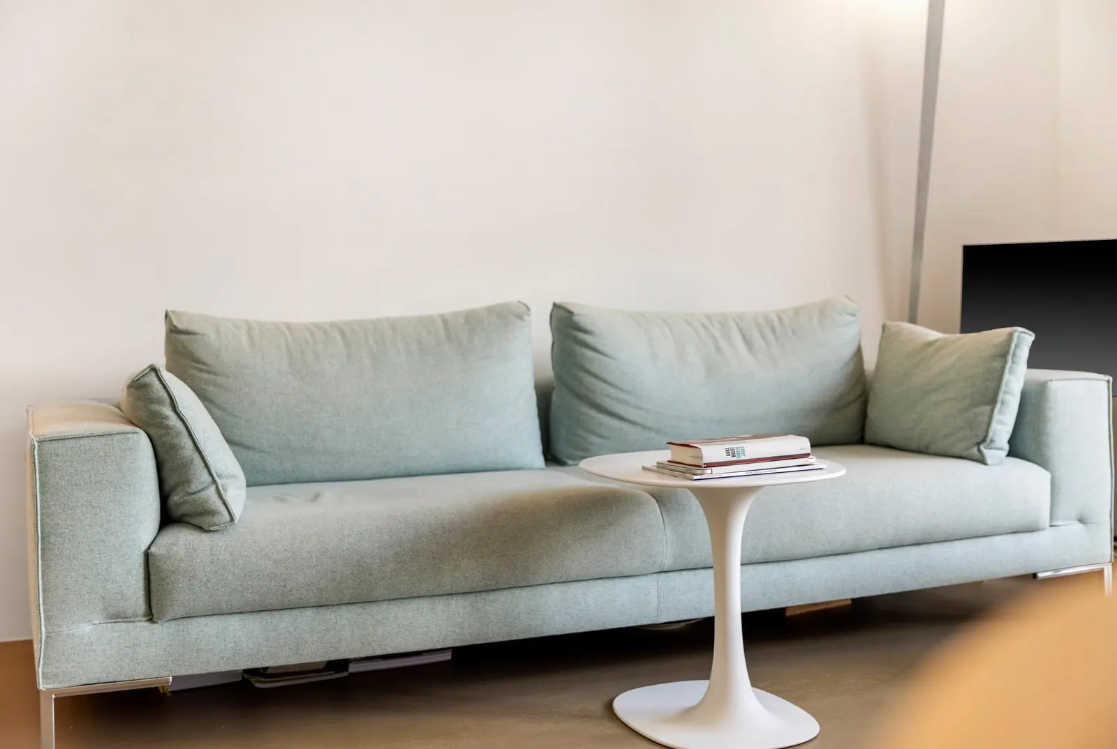 Lichte bank met losse kussens en een witte bijzettafel met enkele boeken in de woonkamer