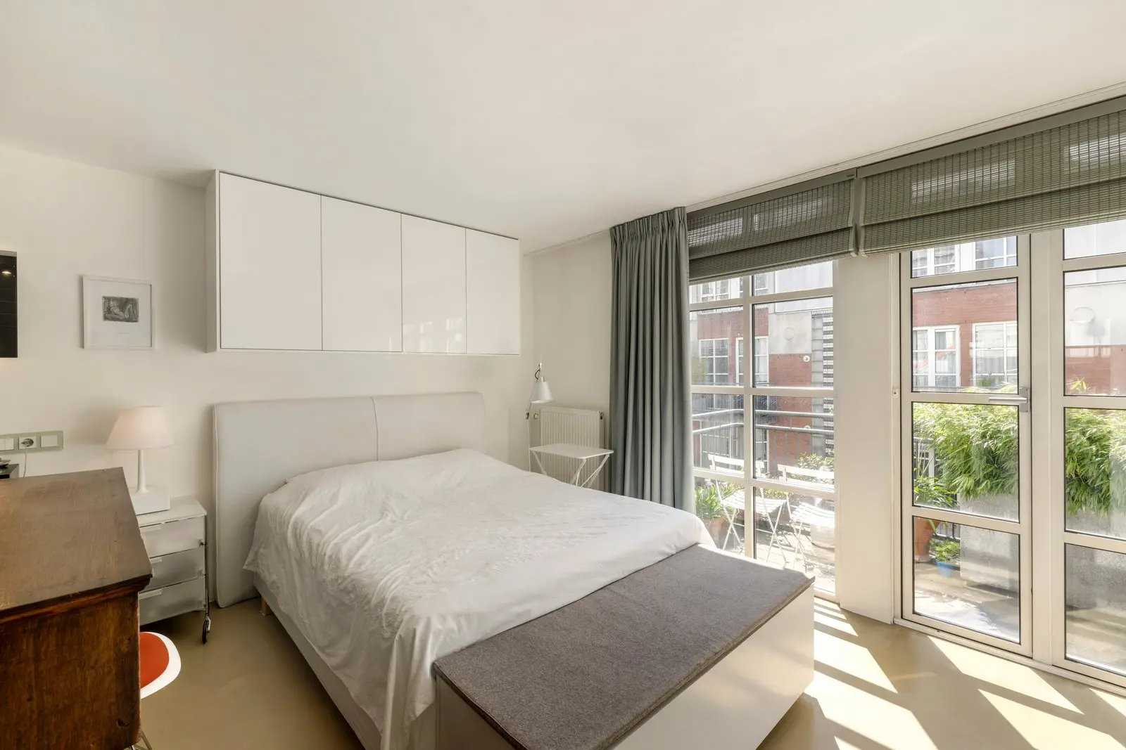 Witte hangkasten boven het bed in de slaapkamer, met kamerhoge ramen en een deur naar het balkon
