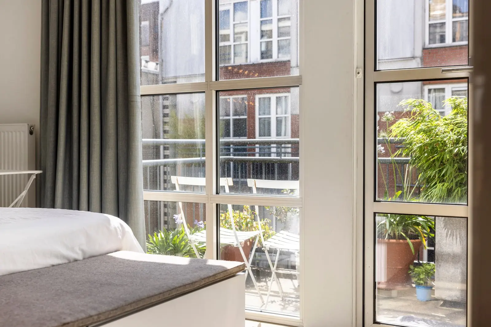 Vanuit de slaapkamer de deur naar het balkon met twee witte stoelen en enkele planten