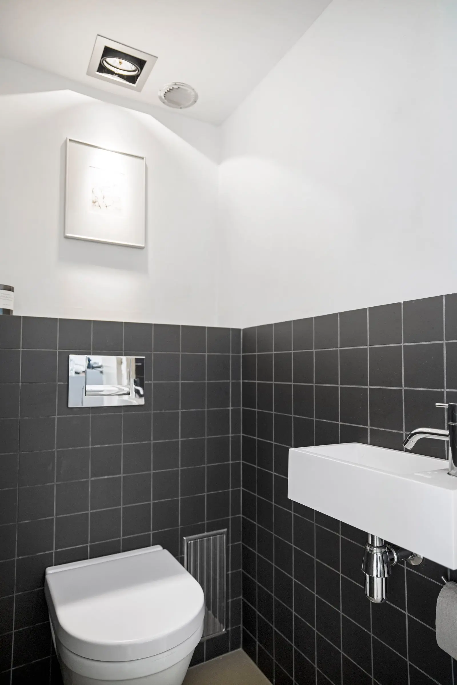 Separaat toilet met donkere wandtegels, wit erboven en een klein fonteintje met chromen kraan