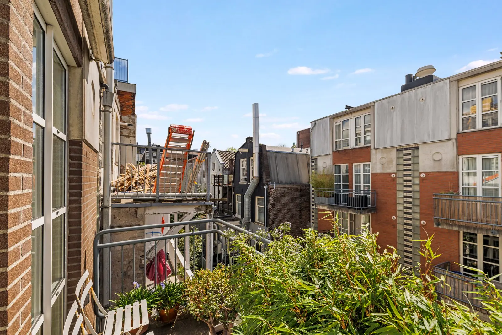 Uitzicht vanaf het balkon op de omliggende gebouwen, met op de voorgrond potplanten en een witte stoel
