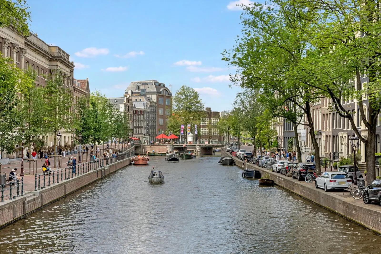 Zicht over de gracht naar een brug, met boten op het water en auto's langs de kade