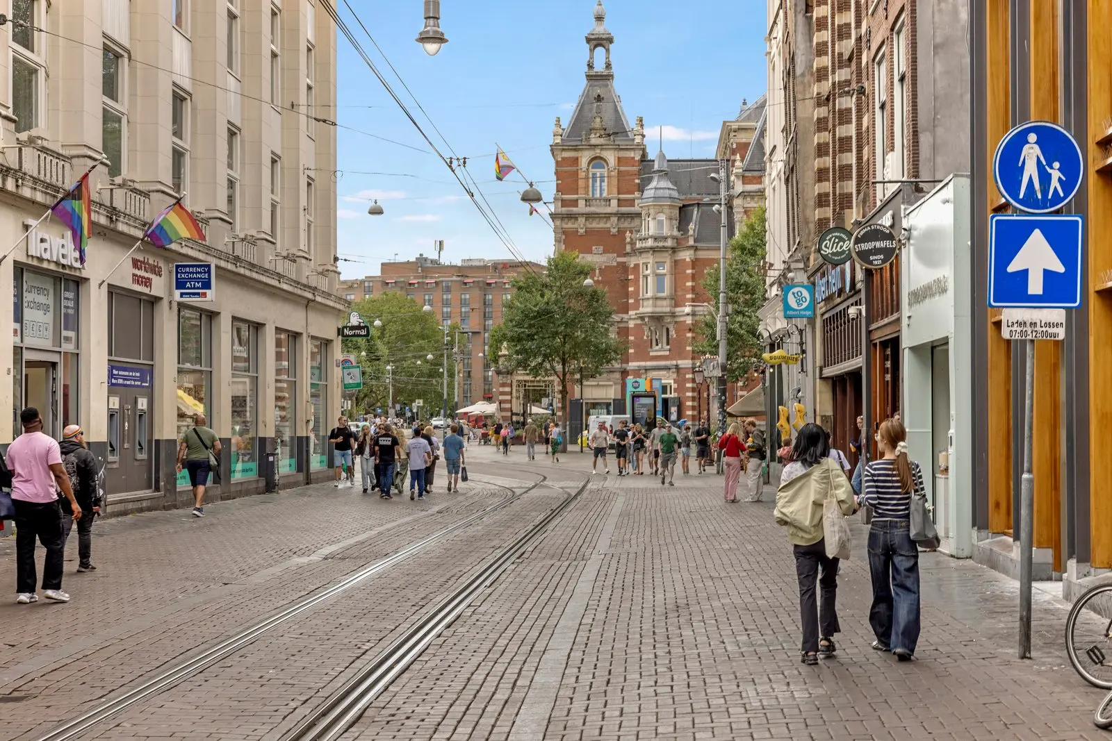 Winkelstraat met tramrails en voetgangers, aan het einde een bakstenen gebouw met torentje