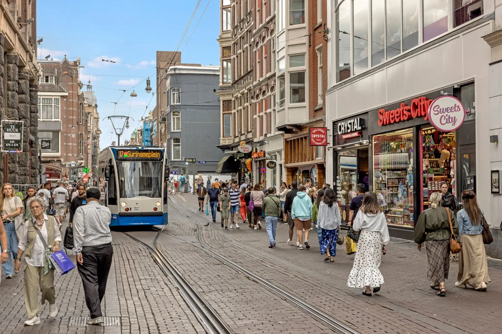 Tram op de rails in een winkelstraat met veel voetgangers langs de winkels