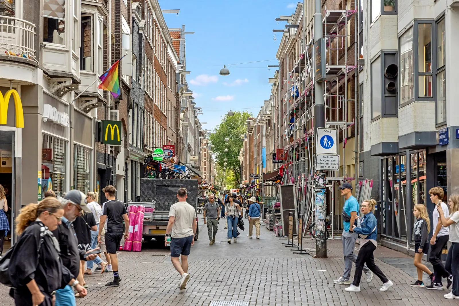 Voetgangers in een straat met links een McDonald's en rechts een steiger tegen de gevel