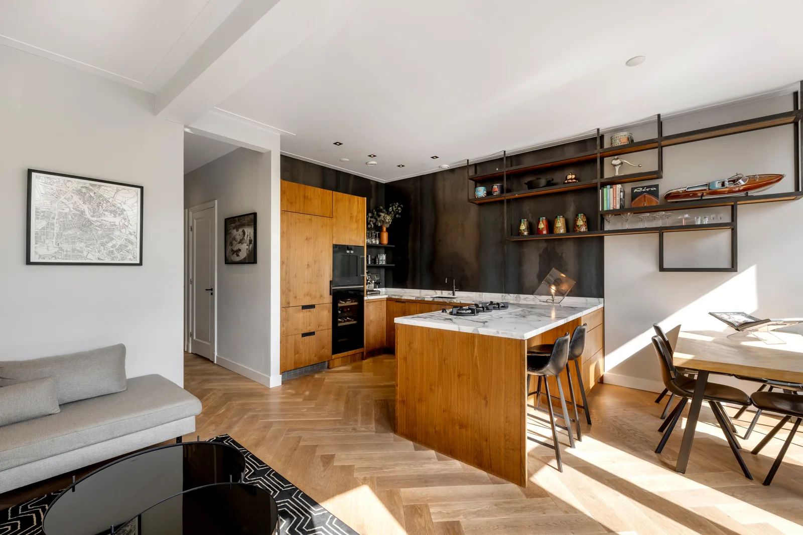 Open keuken met houten fronten tegen donkere wand, kookeiland met marmeren blad en gaskookplaat op visgraatvloer