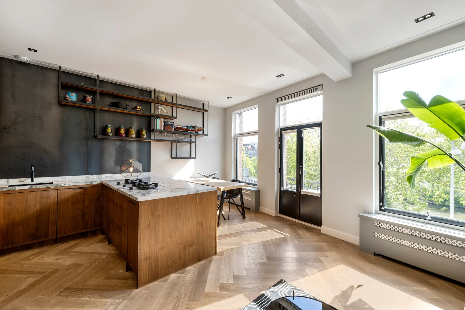 Houten keuken met marmeren blad, open schappen tegen een donkere wand en verderop de eettafel