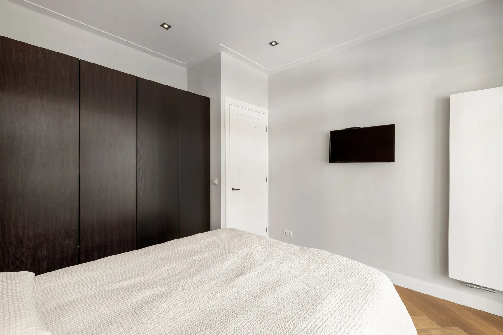 Slaapkamer met bed voor een kastenwand van donkerbruine houten deuren, televisie aan de muur
