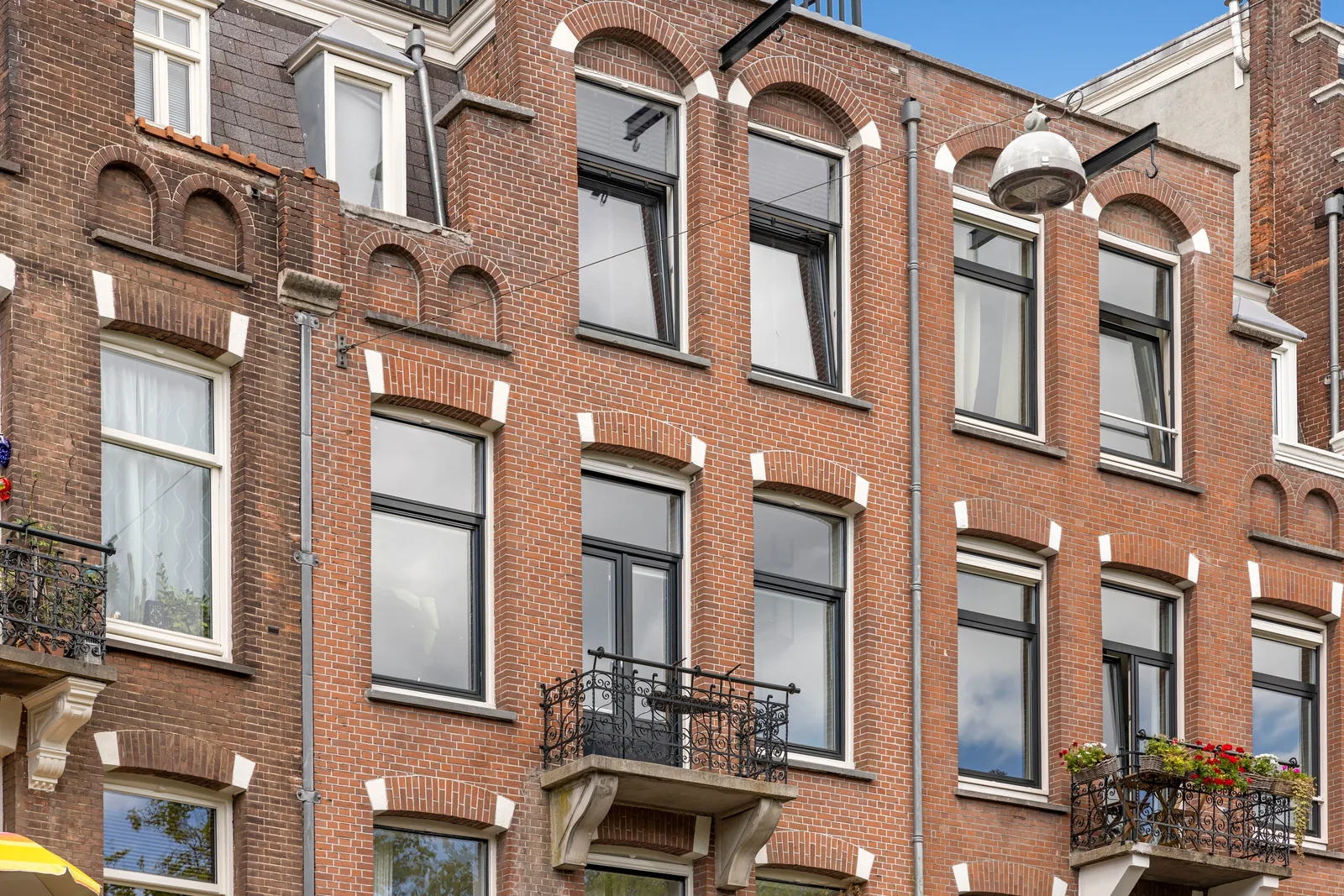 Rode bakstenen gevel met boogramen en twee balkons met zwarte smeedijzeren hekken en bloembakken