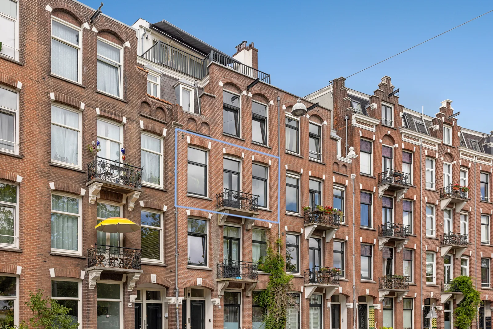 Bakstenen gevelrij, de woning blauw omlijnd op de tweede verdieping met balkon en twee ramen