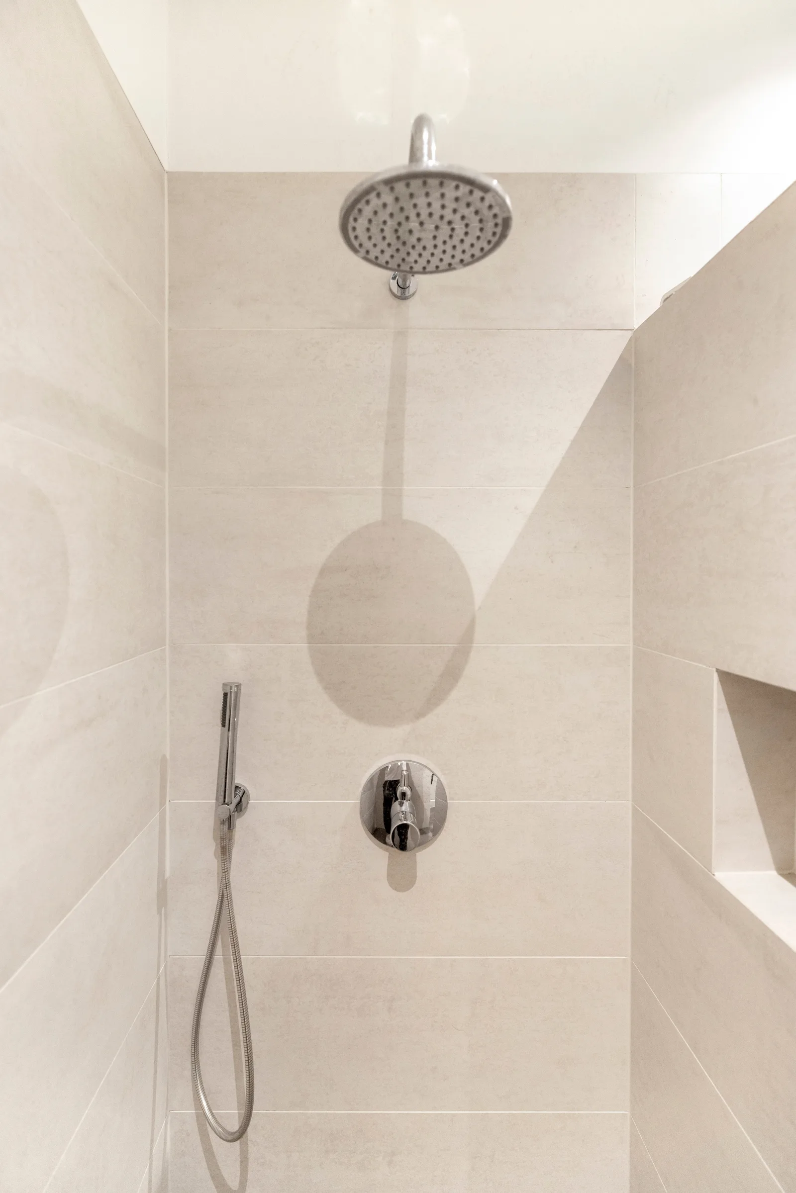 Betegelde douche in beige met ronde regendouche, losse handdouche en een nis in de wand