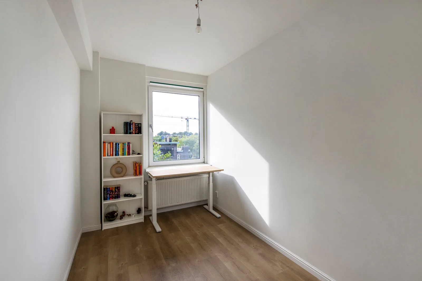 Kamer met witte boekenkast en een in hoogte verstelbaar bureau voor het raam