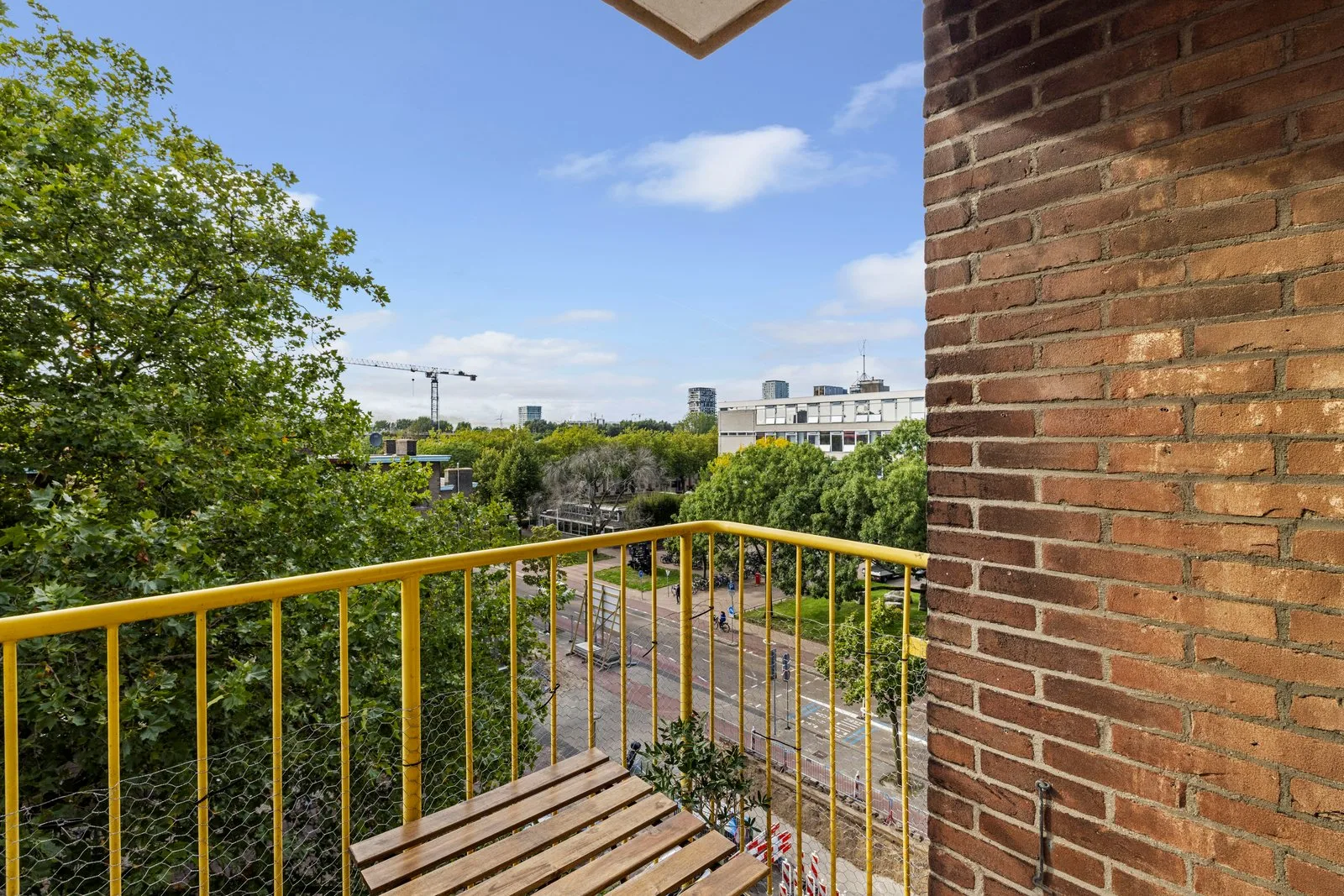 Uitzicht vanaf het balkon over de bomen op de weg en de hoogbouw erachter