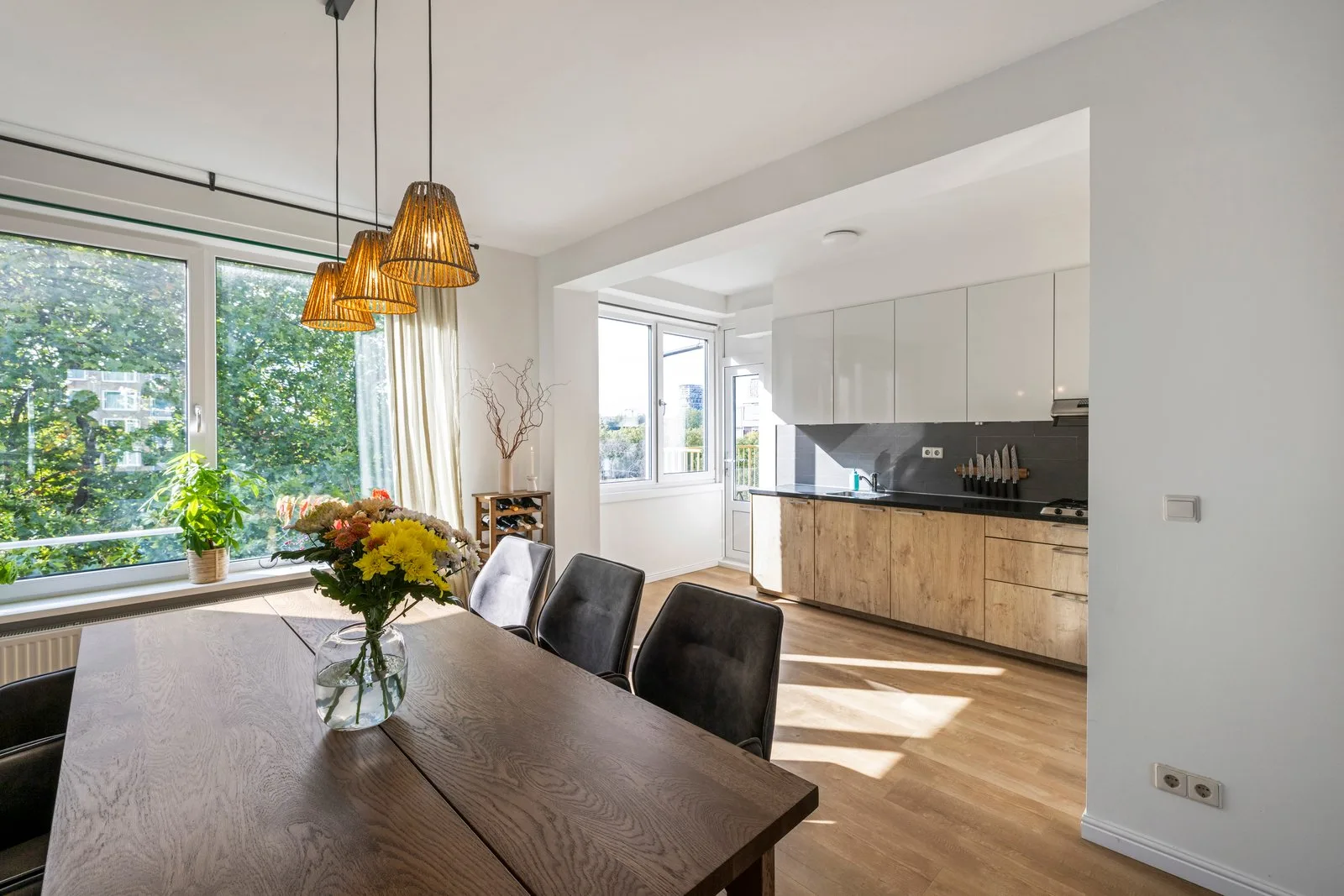 Eettafel met drie rieten hanglampen, daarachter de keuken in het verlengde