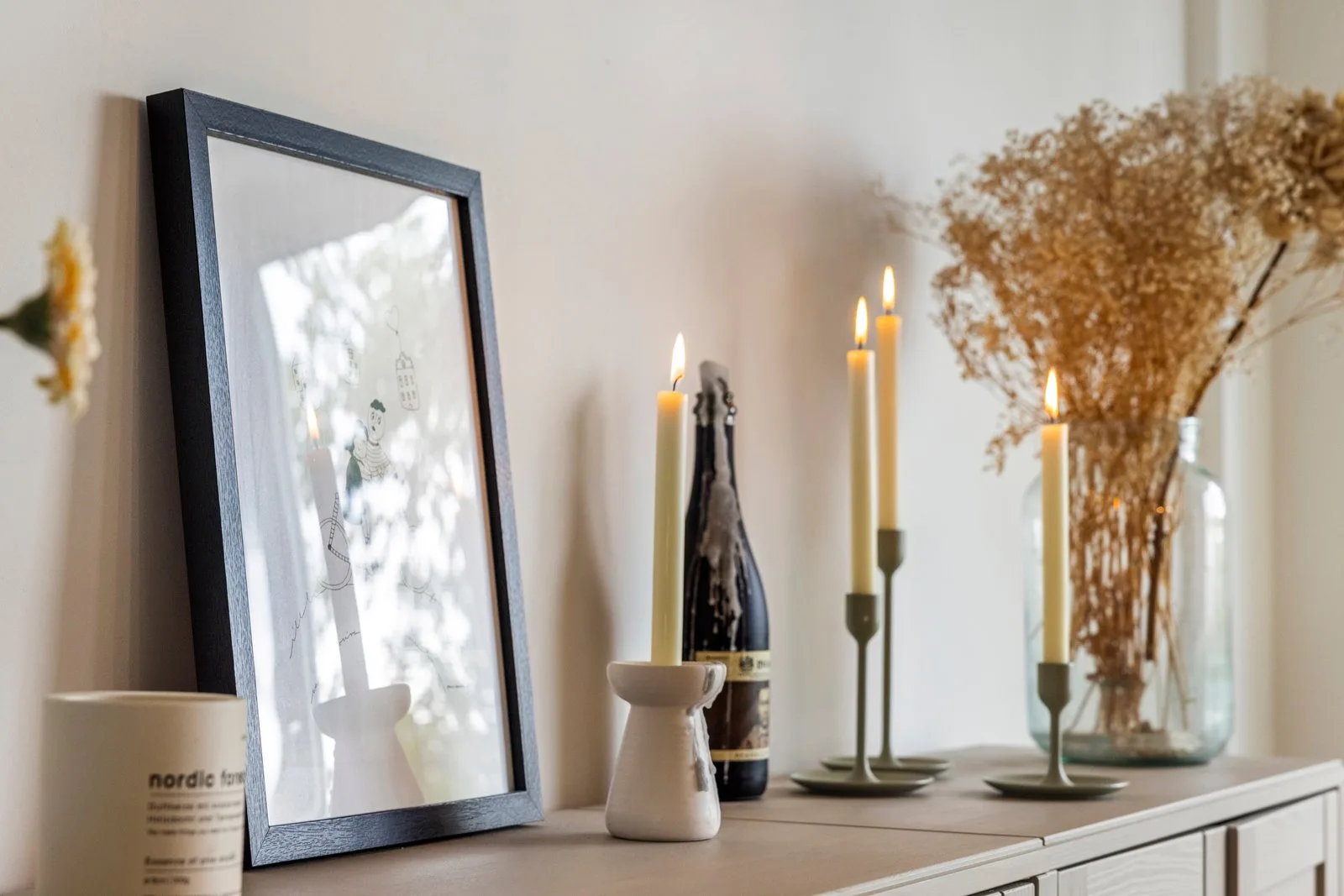 Kandelaars met kaarsen, droogbloemen en een ingelijste tekening op het dressoir