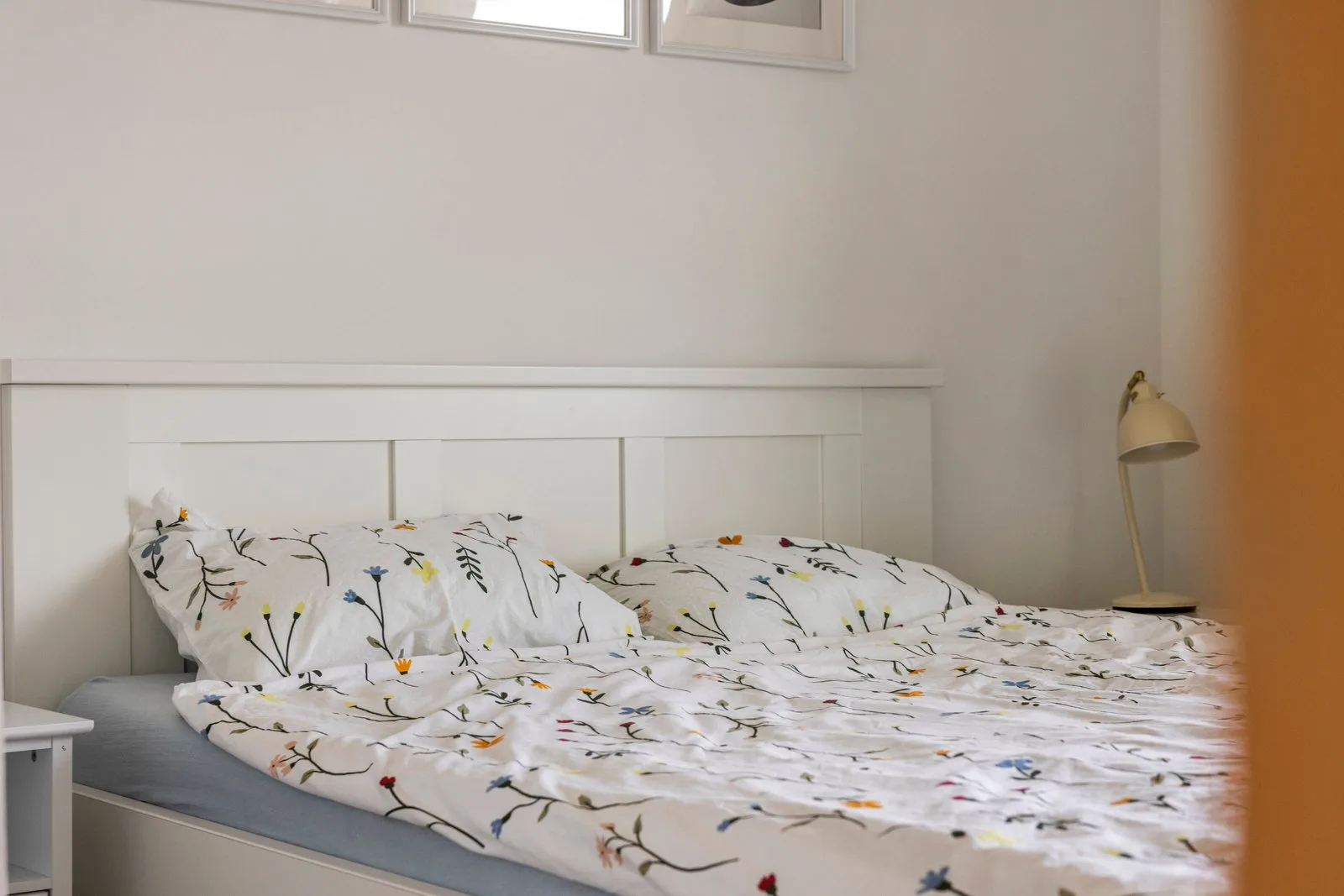 Wit houten hoofdbord, gebloemd dekbed en een leeslamp op het nachtkastje
