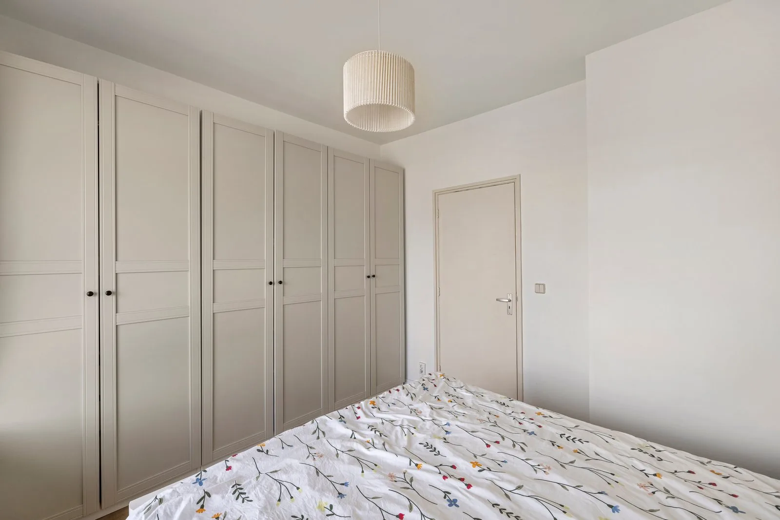 Slaapkamer met een beige kastenwand van vloer tot plafond naast het bed