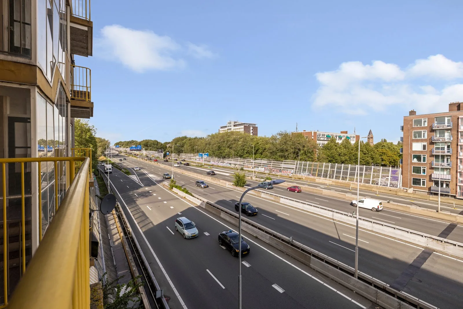 Uitzicht vanaf het balkon over de snelweg, met verderop bomen en een kerktoren