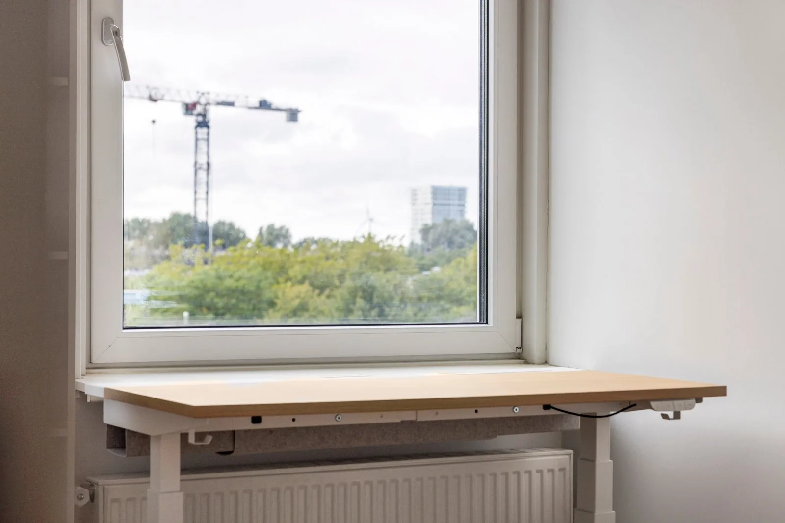 Het verstelbare bureau van dichtbij, door het raam bomen en een bouwkraan