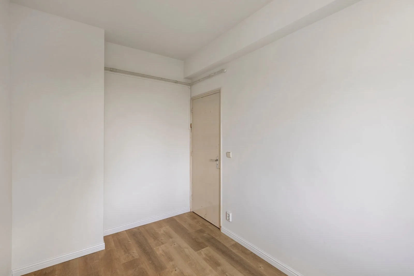 Leeg vertrek met houtlook-vloer, crèmekleurige paneeldeur en een gordijnrail langs de wanden