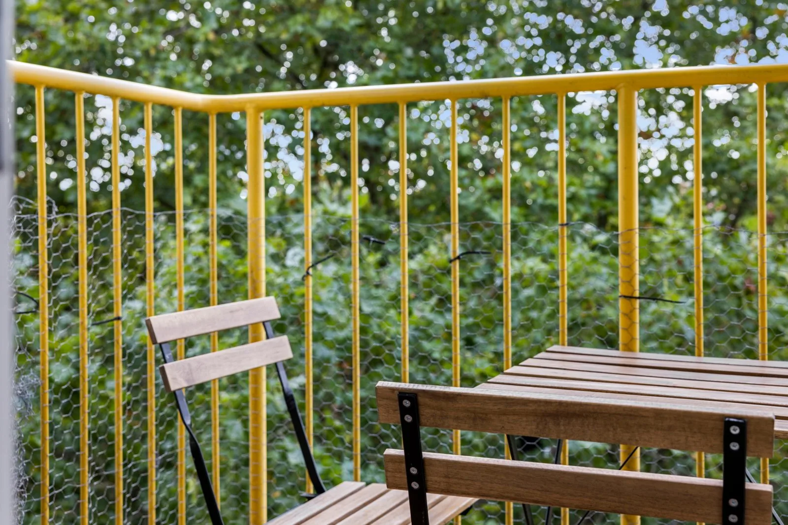 Houten klaptafel en klapstoel op het balkon, gaas tegen het gele hek