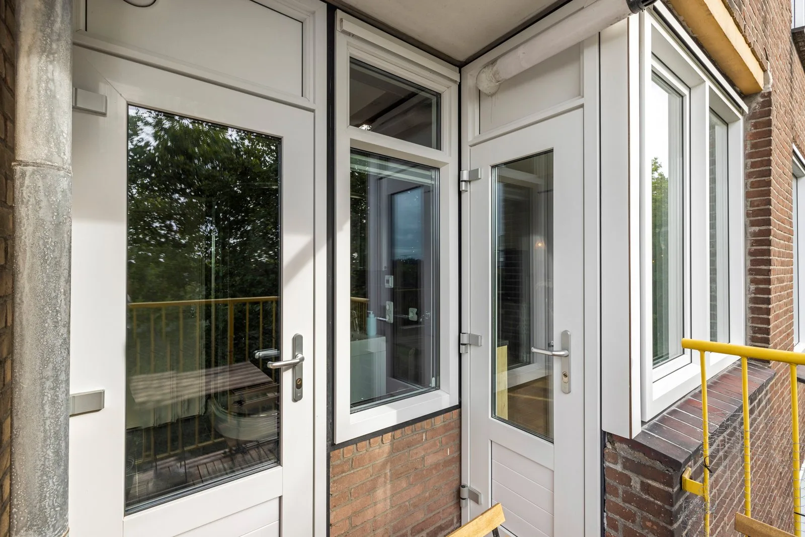 Twee witte balkondeuren met daartussen een openstaand raam in de bakstenen gevel