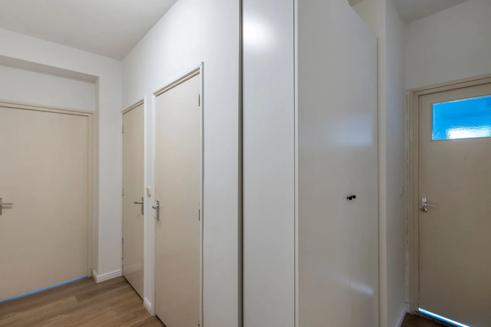 Hal met houtlook-vloer, een inbouwkast tot het plafond en crèmekleurige deuren