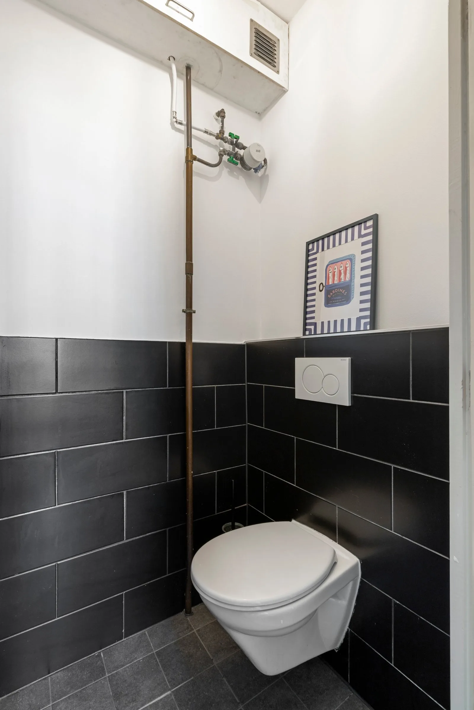Hangend toilet met zwarte wandtegels tot halve hoogte en een ingelijste poster