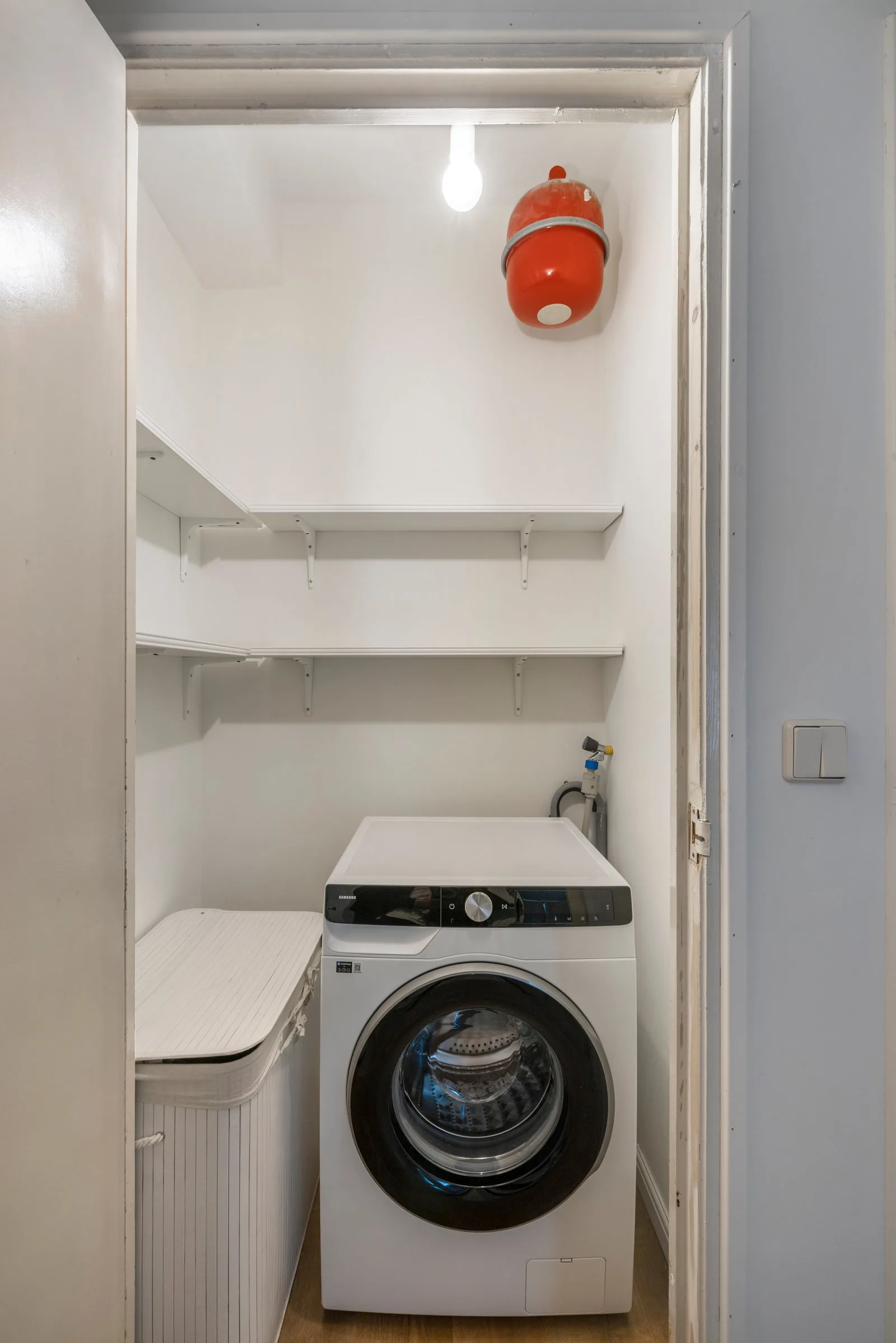 Inloopbergkast met twee wandplanken, daaronder de wasmachine en een rieten wasmand