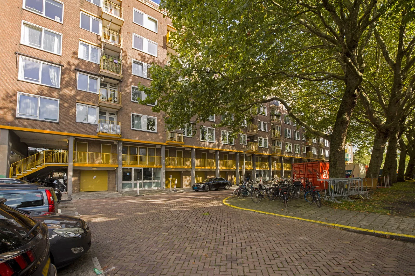 Het gebouw vanaf de parkeerplaats, met bergingen, garagedeur en de gele buitentrap